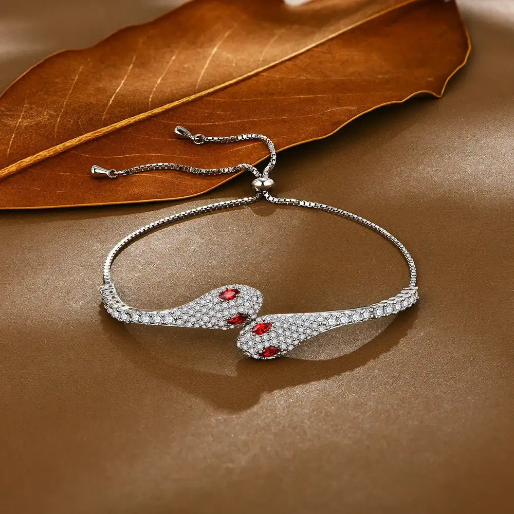 Moissanite twin snake bracelet in a white gold finish on a warm brown surface beside a dried leaf showing the box chain and slider - Sensitive Stones
