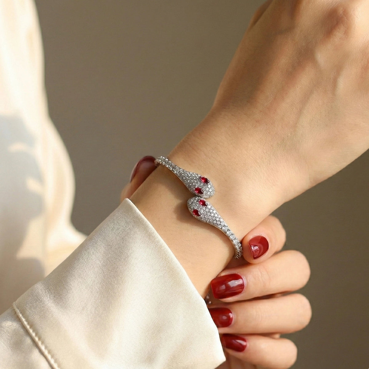 Woman wearing a moissanite twin snake bracelet in a white gold finish on her wrist with a cream silk sleeve - Sensitive Stones
