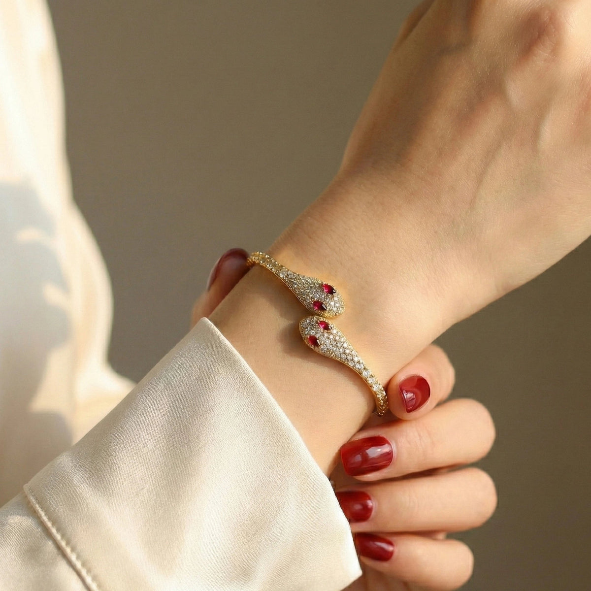 Woman wearing a moissanite twin snake bracelet in a yellow gold finish on her wrist with a cream silk sleeve - Sensitive Stones