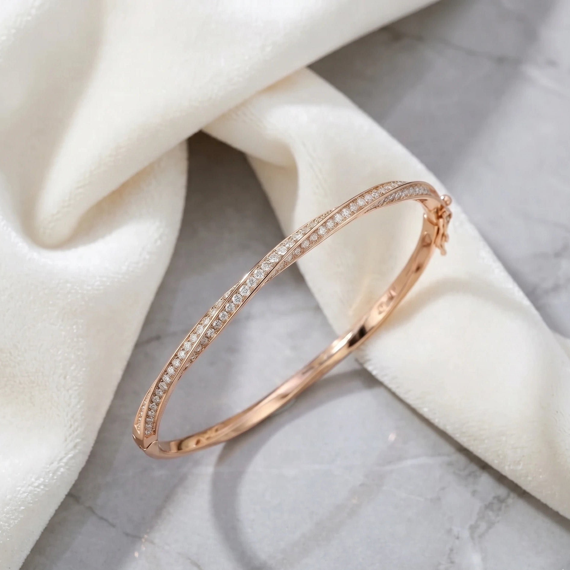 Moissanite twist bangle in 18K rose gold on marble surface with white fabric - Sensitive Stones