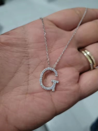 Hand holding a rhodium-plated 925 sterling silver necklace featuring a pavé lab-created moissanite ‘G’ initial pendant