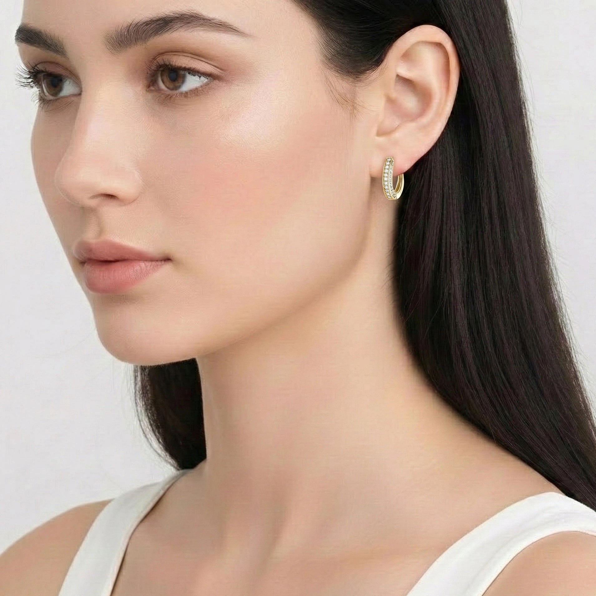 Close-up of a woman wearing yellow gold moissanite huggie hoop earrings against a white background - Sensitive Stones