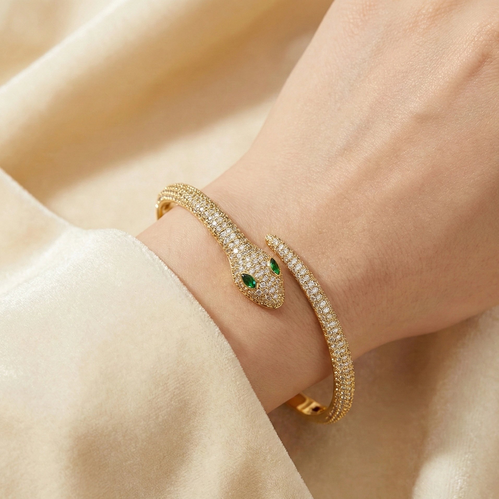 Moissanite snake bracelet with 18k gold finish with green eyes on a wrist against a beige background - Sensitive Stones