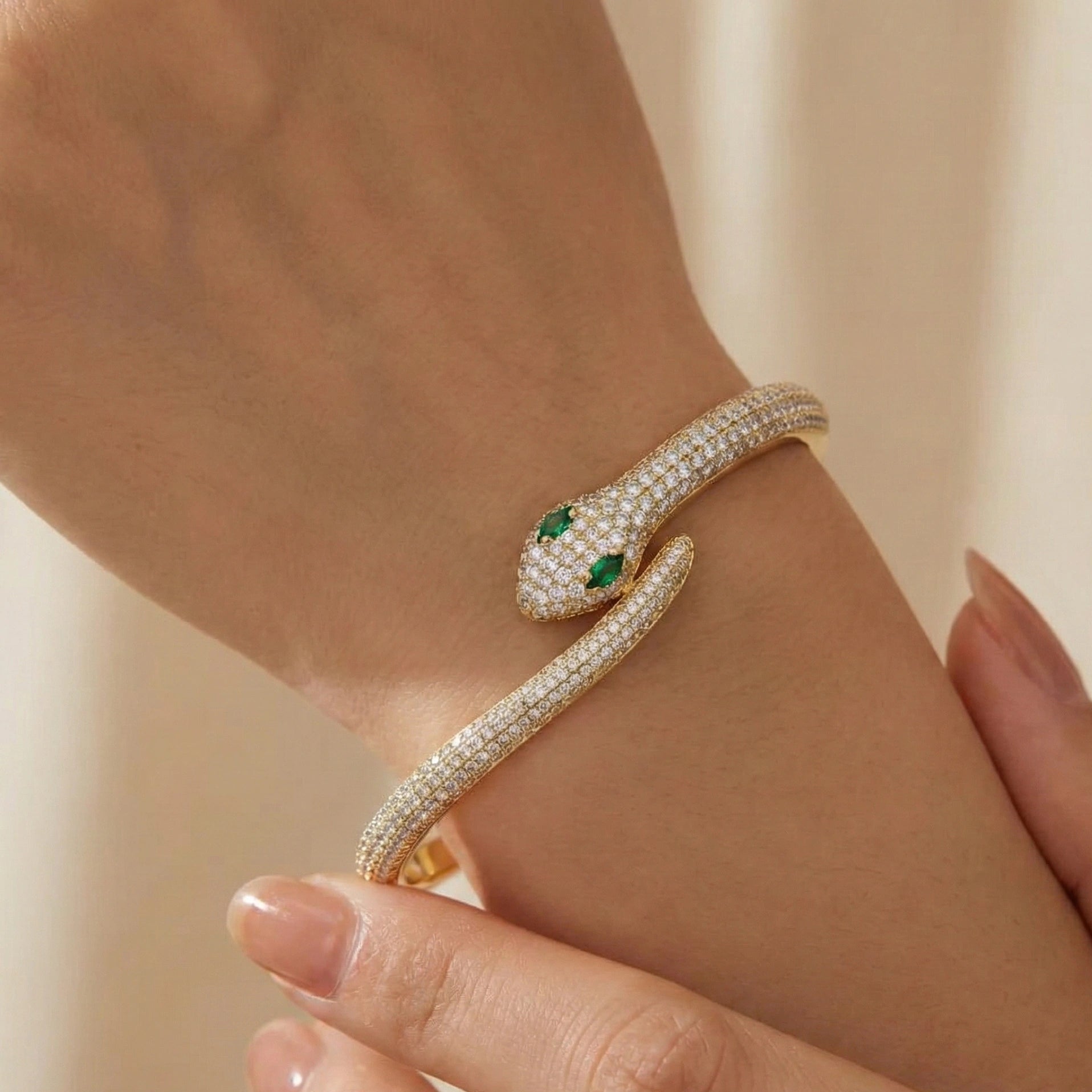 Moissanite snake bracelet with 18k gold finish with green eyes on a wrist against a beige background - Sensitive Stones