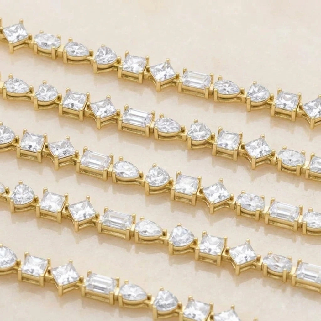 Close up of multiple multi shape moissanite tennis bracelet strands in yellow gold showing prong set pear, heart, princess, oval and emerald cut stones - Sensitive Stones