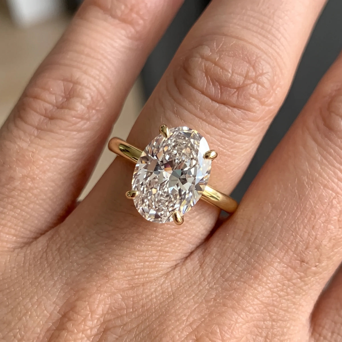 Close-up of a hand wearing the oval cut moissanite solitaire ring in a yellow gold finish - Sensitive Stones