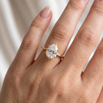 Close-up of a 2ct pear cut moissanite engagement ring in 14K gold filled worn on the finger, showing the six prongs and the V-tip capping the point - Sensitive Stones