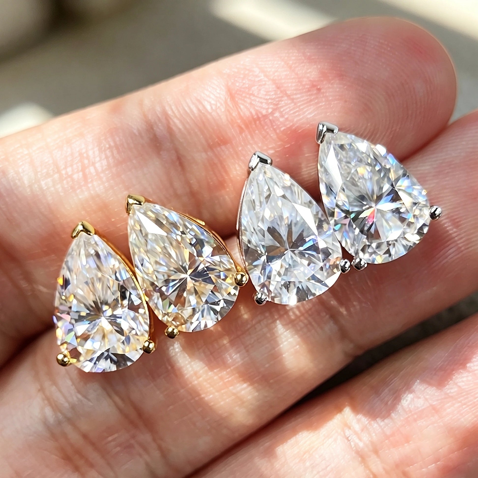 Four pear cut moissanite studs held in daylight, yellow gold and white gold, showing the carat size range