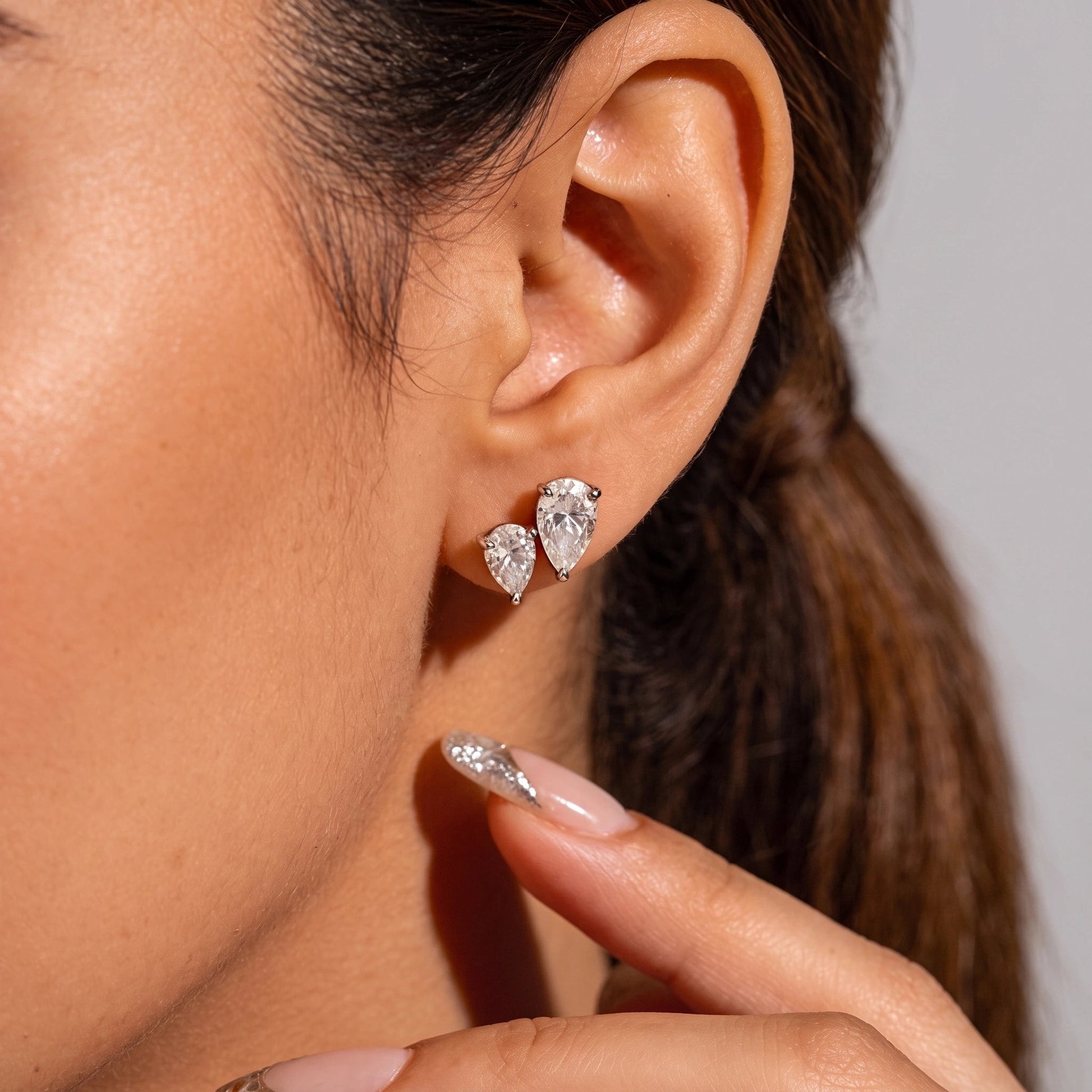 Two white gold pear cut moissanite studs worn point down in stacked lobe piercings