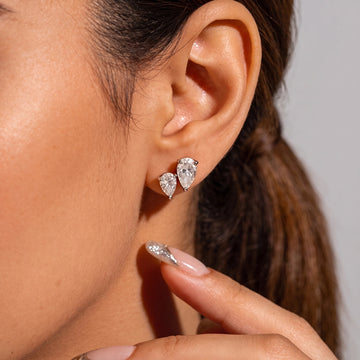 Two white gold pear cut moissanite studs worn point down in stacked lobe piercings