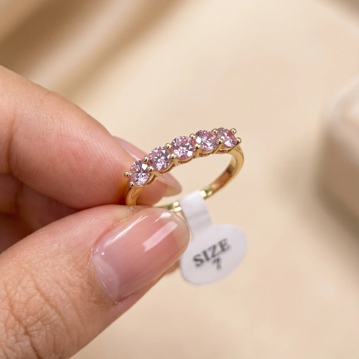 Pink moissanite five stone stackable ring in 14K gold filled held between fingers with a US size 7 tag, showing the slim band profile - Sensitive Stones