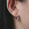 Model wearing 3CT oval moissanite huggie hoop earrings in sterling silver and gold plating, showing elegant sparkling center stones and CZ accents in both color options - Sensitive Stones