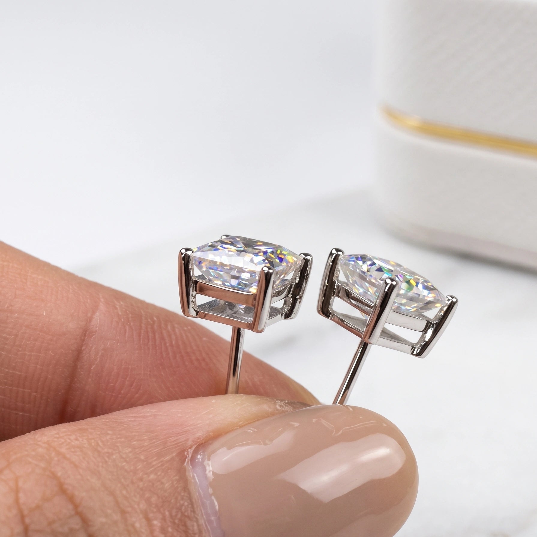 Princess cut moissanite stud earrings in white gold held in hand - Sensitive Stones