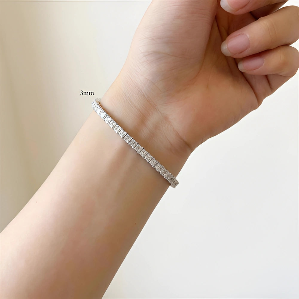 Woman wearing a 4mm princess cut moissanite tennis bracelet, hand resting on white bedding in warm morning light - Sensitive Stones