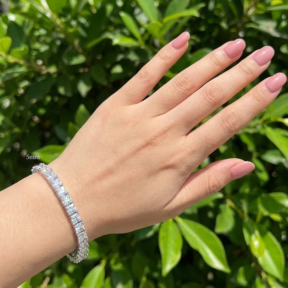 Woman wearing a 5mm princess cut moissanite tennis bracelet with hand outstretched against a green garden hedge - Sensitive Stones