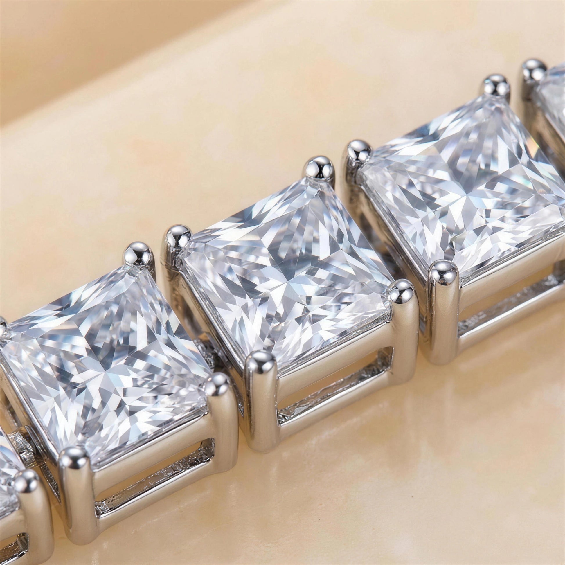 Macro close-up of princess cut moissanite tennis bracelet showing square D Color VVS1 stones in four-prong claw settings on a cream background - Sensitive Stones