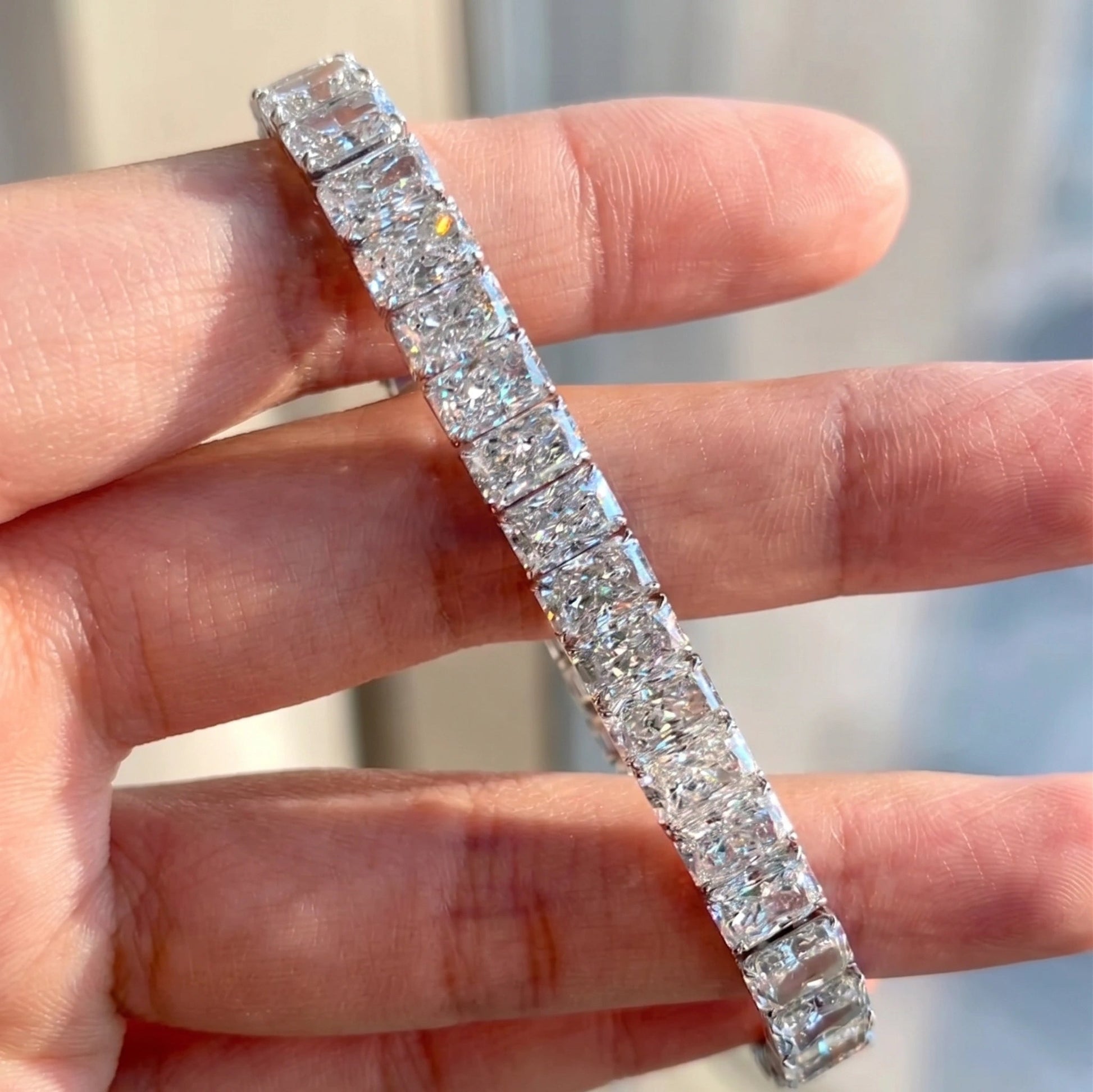 Radiant cut moissanite tennis bracelet held in natural daylight showing its continuous line of stones