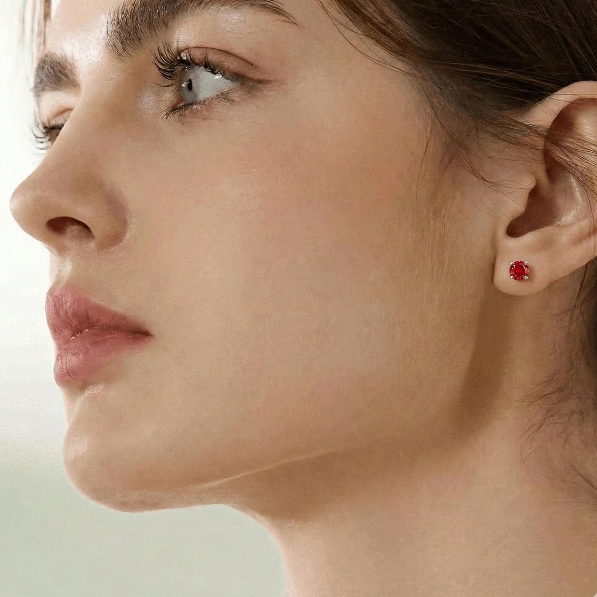 Close-up of a red moissanite stud earring worn on a woman's ear, round cut, 4-prong setting - Sensitive Stones