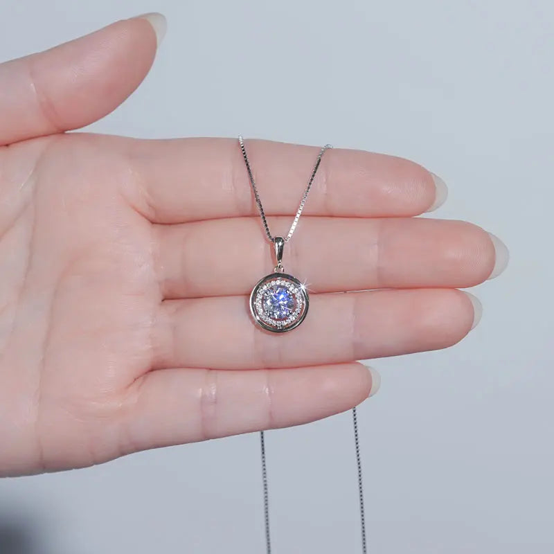 Round moissanite halo pendant necklace in a white gold finish held in the palm to show the pendant size - Sensitive Stones
