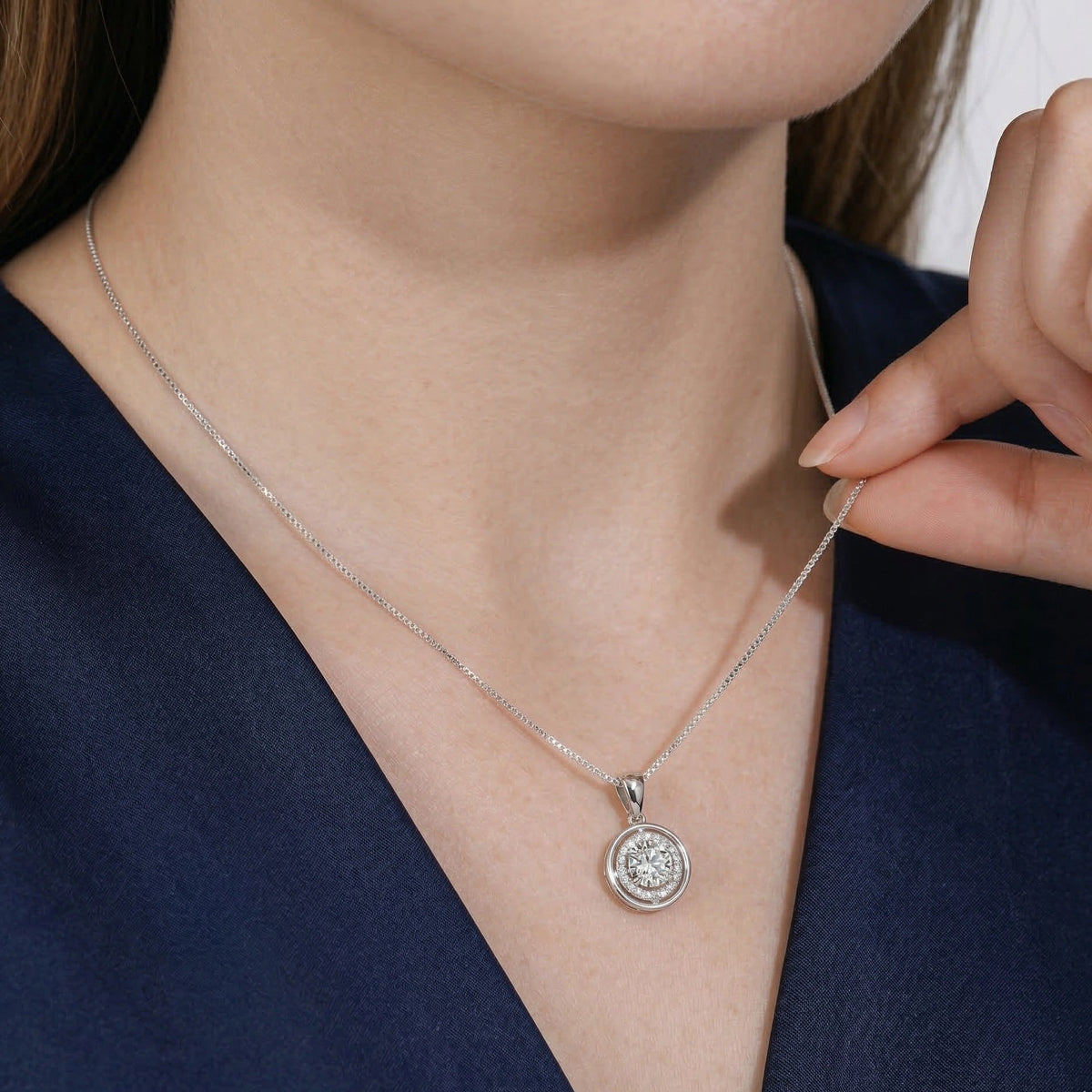 Woman wearing a round moissanite halo pendant necklace in a white gold finish with a navy top - Sensitive Stones