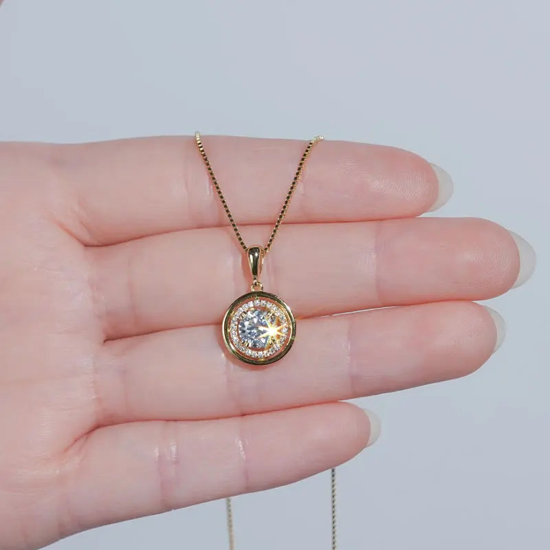 Round moissanite halo pendant necklace in a yellow gold finish held in the palm to show the pendant size - Sensitive Stones