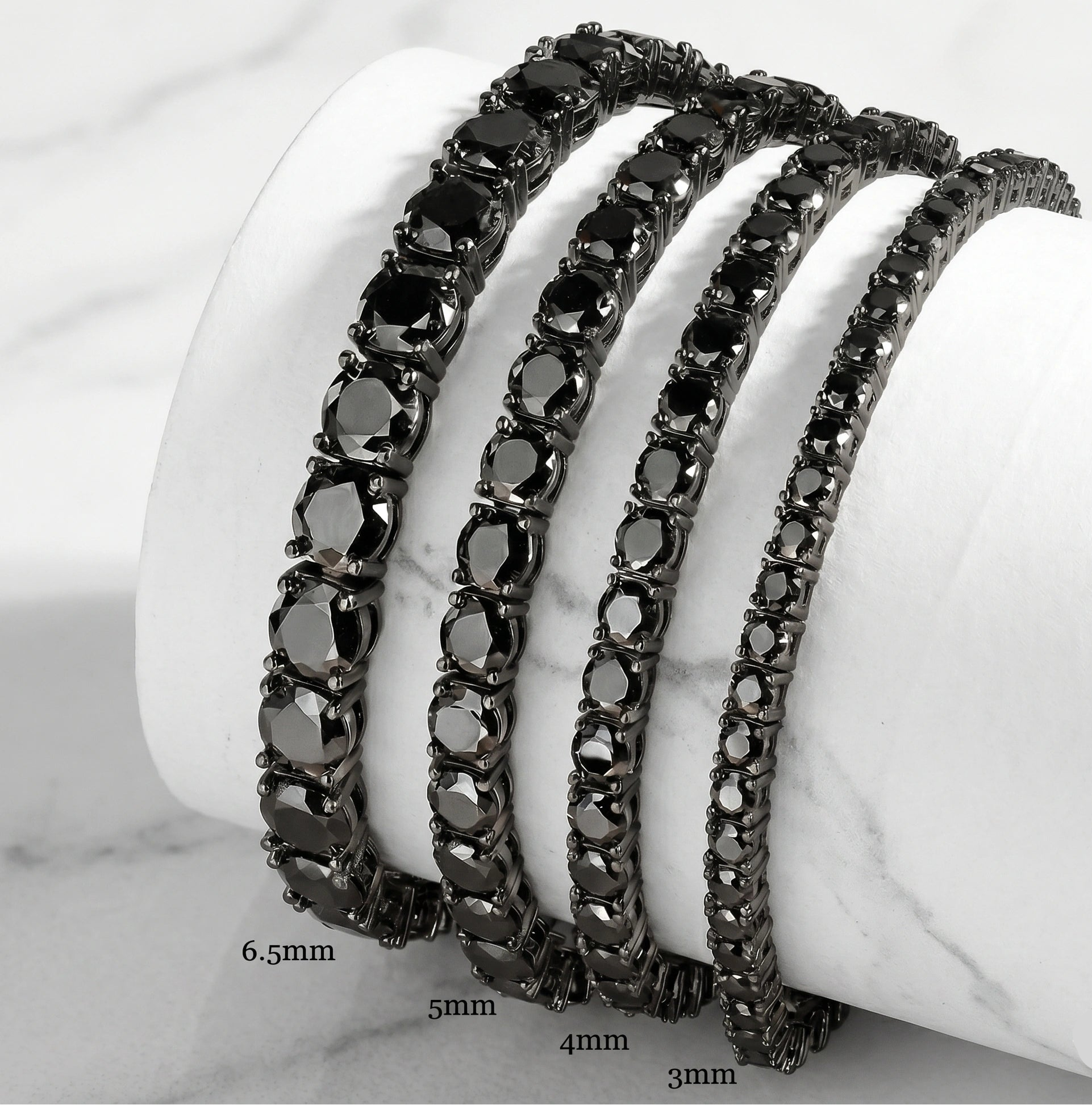 Set of black moissanite tennis bracelets in black gold plating on a white stand with sizes 3mm, 4mm, 5mm, 6.5mm - Sensitive Stones