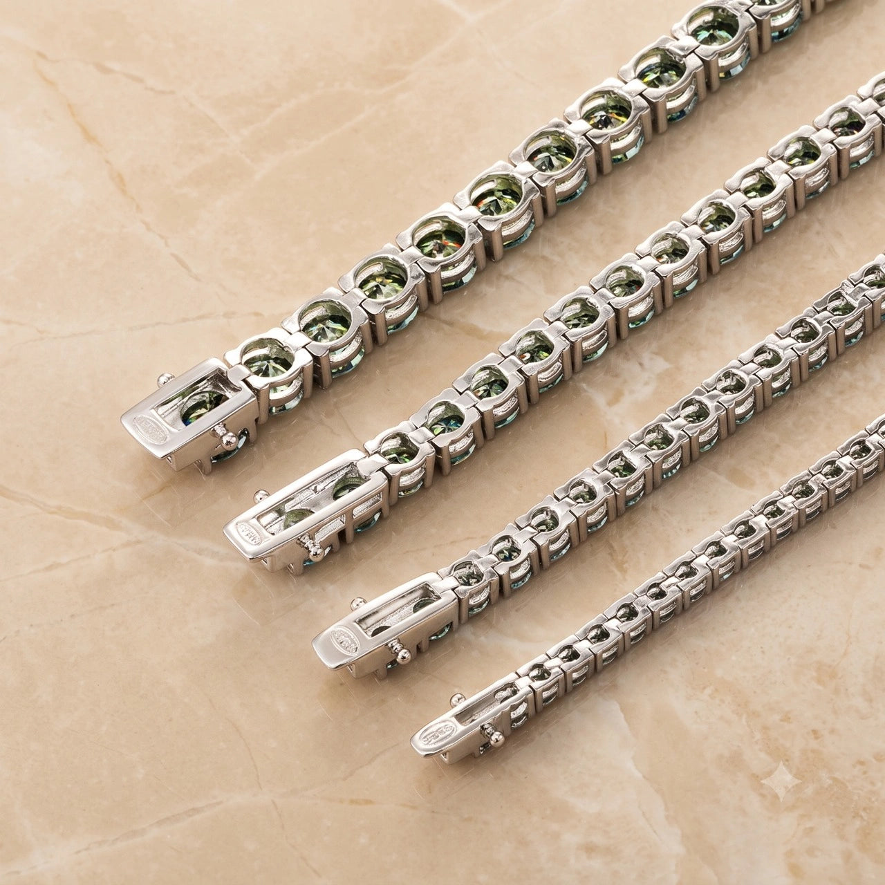 Silver tennis bracelets with round green moissanite, arranged face down diagonally on a beige marble surface - Sensitive Stones