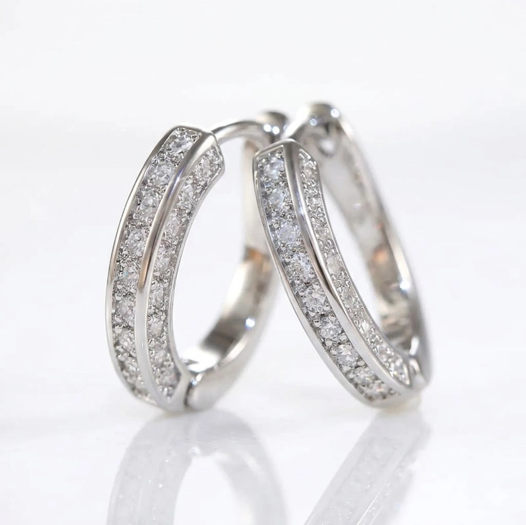 Pair of silver moissanite huggie hoop earrings with embedded stones on a reflective surface - Sensitive Stones