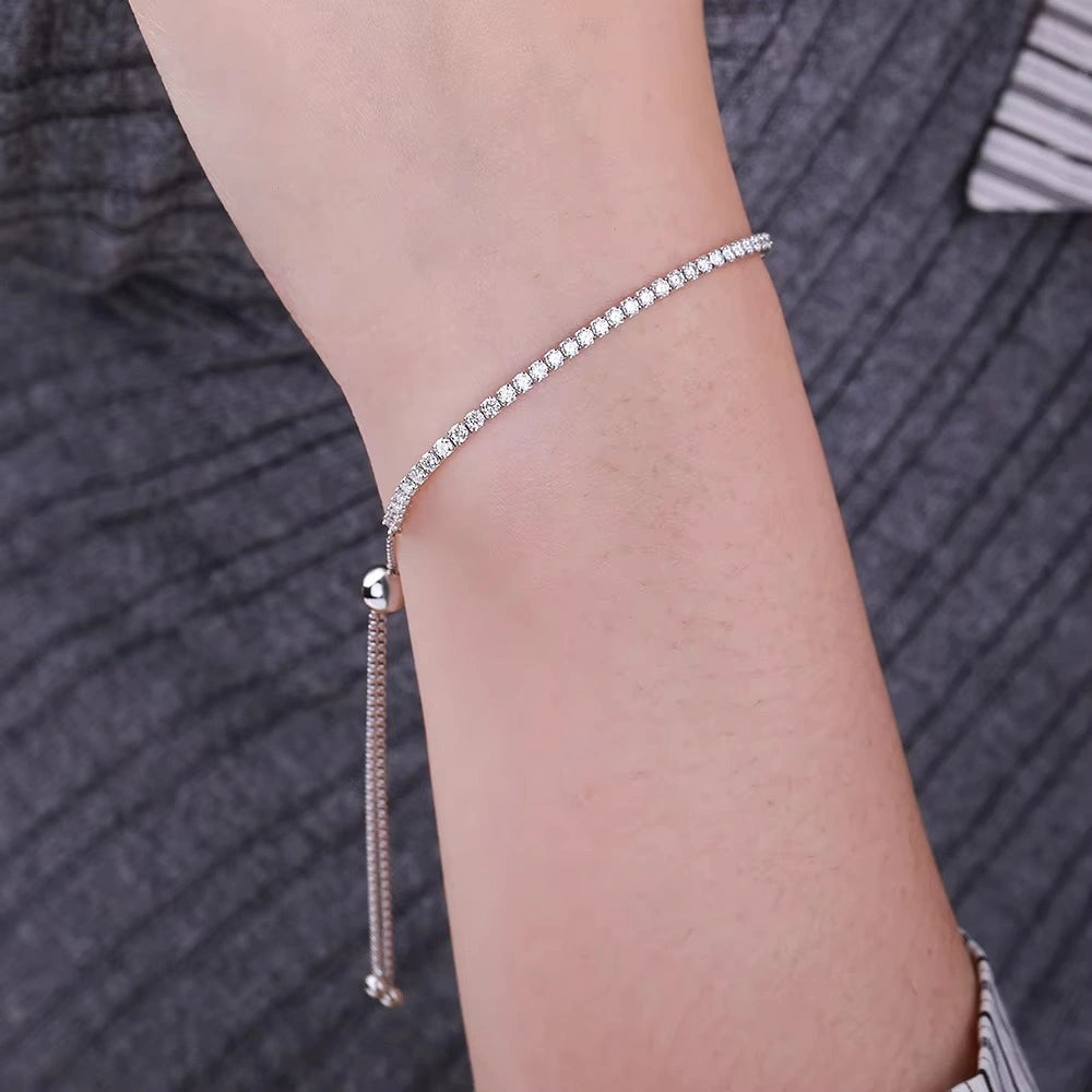 925 sterling silver adjustable bolo tennis bracelet with row of sparkling round moissanite stones and sliding ball closure with tassel chain, worn on wrist against grey knit background - Sensitive Stones