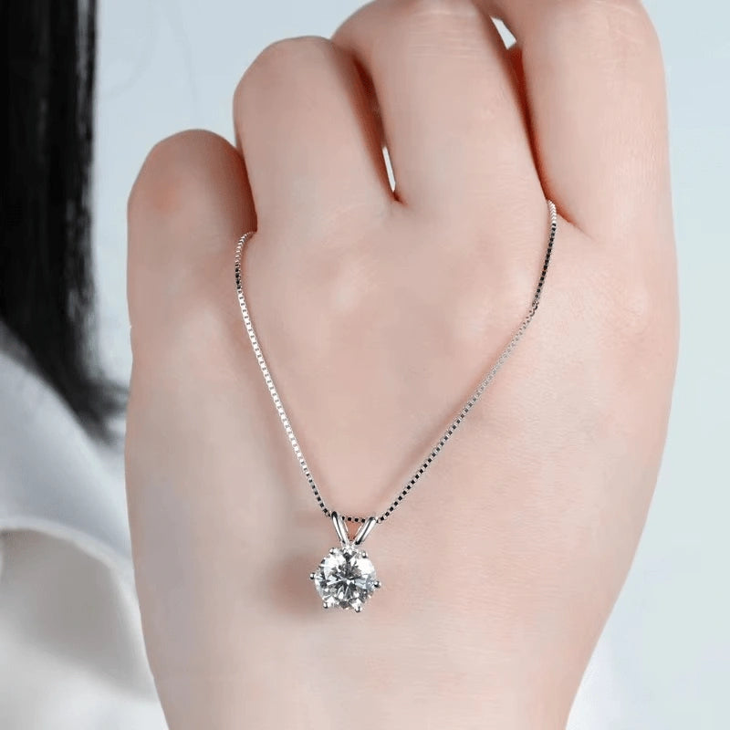 6-prong silver round brilliant cut moissanite solitaire pendant necklace with box chain, professional jewelry photography showing diamond sparkle and setting detail held in hand - Sensitive Stones