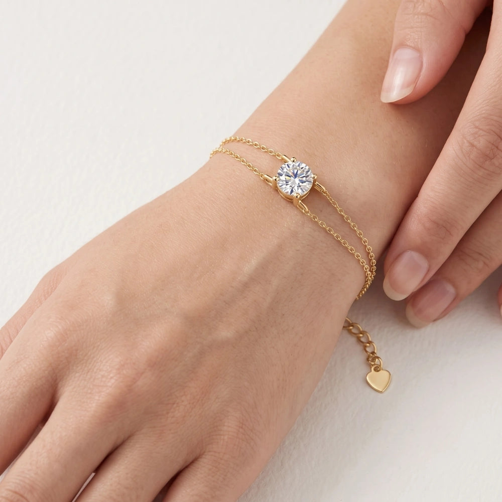 A woman's wrist wearing a yellow gold moissanite solitaire double chain bracelet with a round 1ct D color stone and heart charm extender - Sensitive Stones