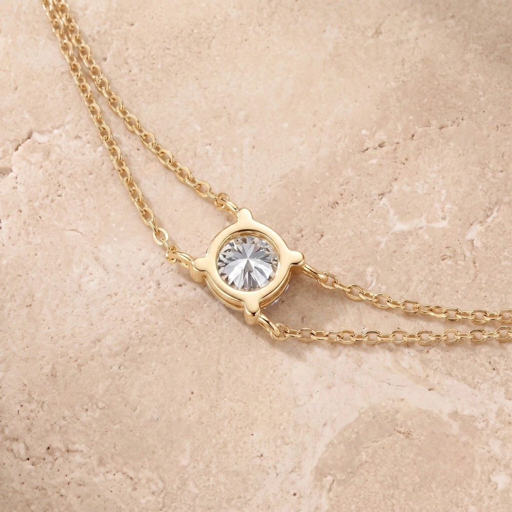 Close-up of a yellow gold moissanite solitaire double chain bracelet showing the 4-prong set round 1ct D color stone - Sensitive Stones
