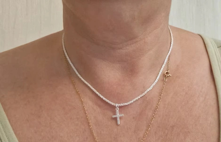 Close-up of sterling silver cross pendant layered with a gold chain
