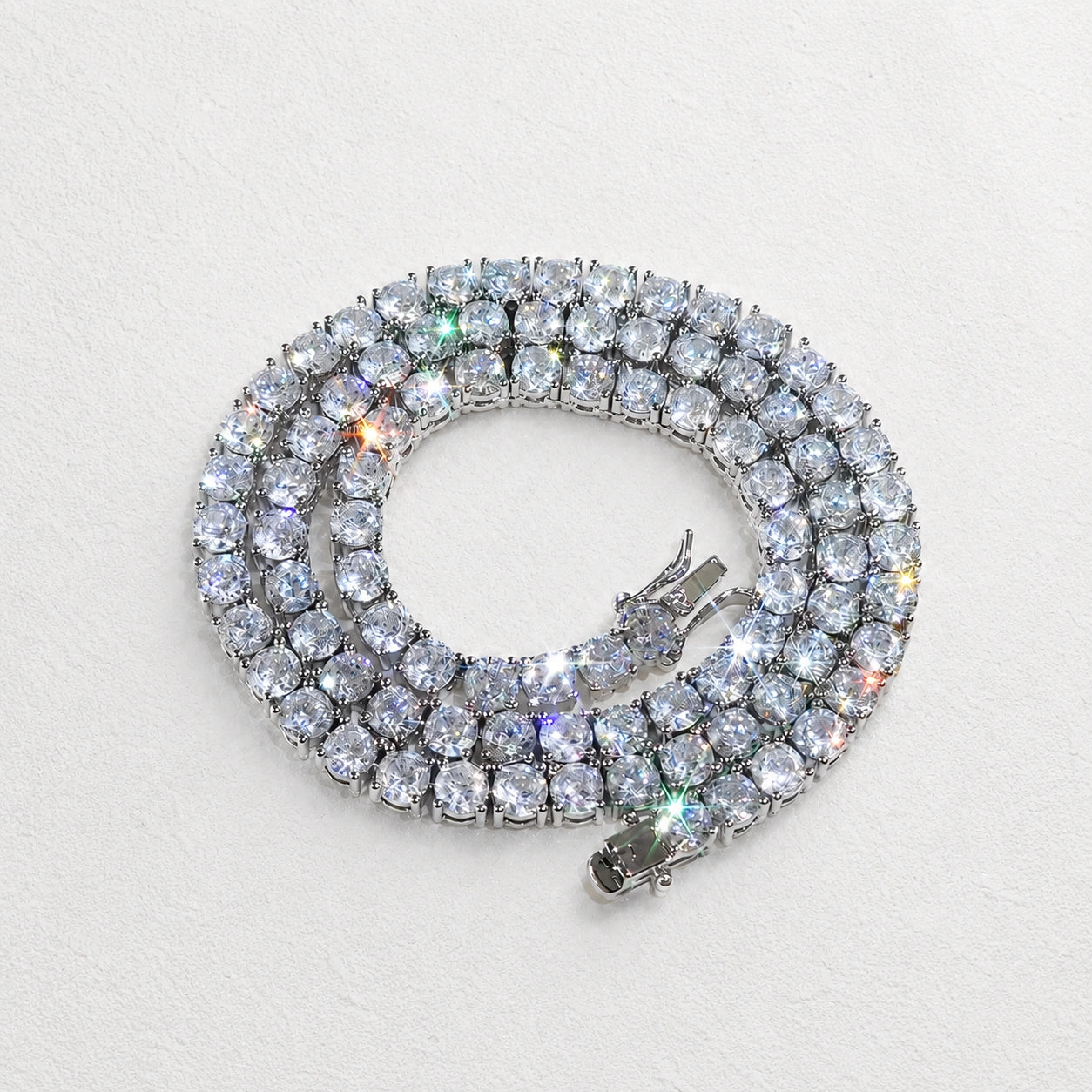 White moissanite tennis necklace in white gold plated 925 sterling silver, coiled flat lay showing rainbow fire, 4-prong round stones - Sensitive Stones