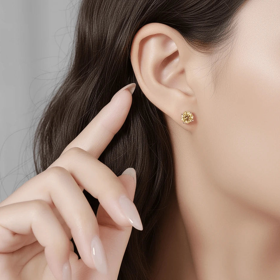 Close-up of a yellow moissanite stud earring worn on a woman's ear, round cut, 4-prong setting - Sensitive Stones
